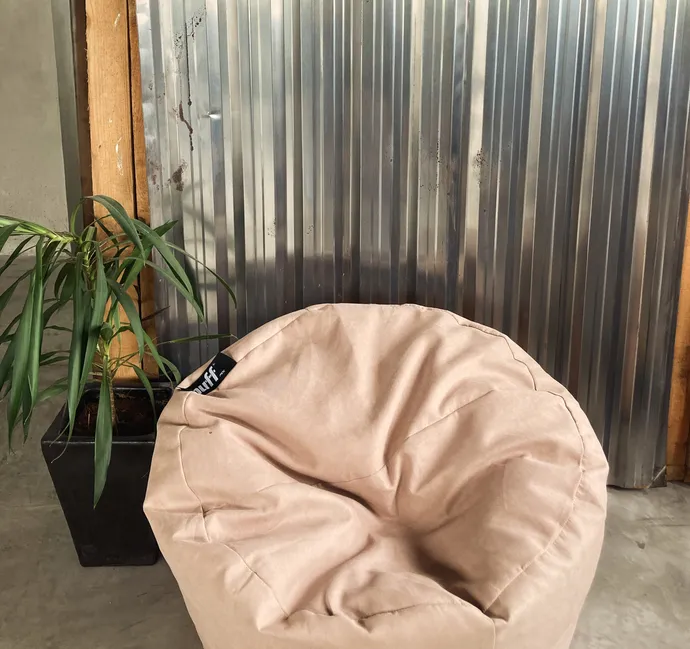 A person sitting on a bean bag chair while working on a laptop in a relaxed environment.
